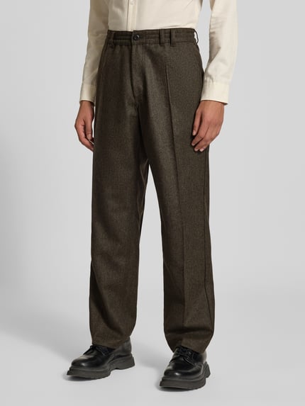 Männermodel trägt Straight Fit Anzughose aus Woll-Mix von Forét in Dunkelbraun mit Bundfalten, Eingriff- und Gesäßtaschen, Ganzkörperansicht von vorne.