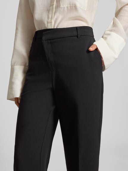 Frauenmodel trägt Regular Fit Hose mit Viskose-Anteil von OPUS in Schwarz mit asymmetrischem Hakenverschluss und französischen Eingrifftaschen, Material-Mix, verkürztes Bein, Nahaufnahme Oberkörper.
