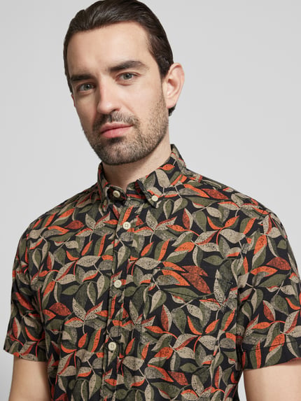 Männermodel trägt Regular Fit Freizeithemd aus reiner Baumwolle von camel active mit Blätterprint in Schwarz, Orange und Beige, Nahaufnahme Oberkörper.