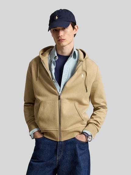Męski model nosi Regular Fit Sweatjacke aus Baumwoll-Mix od Polo Ralph Lauren, kolor beżowy, kieszenie z przodu, gładka tekstura, Ganzkörperansicht von vorne.