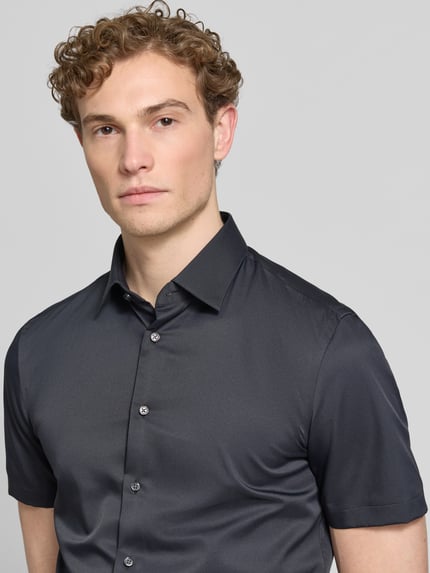 Männermodel trägt Slim Fit Business-Hemd mit Kentkragen von Jake*s, Elastischer-Material-Mix, Knopfleiste, Kurzärmelig, Nahaufnahme Oberkörper.