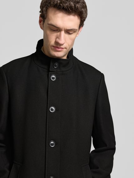 Mannenmodel draagt Mantel mit Stehkragen und Eingrifftaschen van Christian Berg Men, zwart, slim fit, mix van materialen met stretch, knoopsluiting, borstbreedte 60 cm, schouderbreedte 47 cm, lengtemaat 100 cm, mouwlengte 69 cm, close-up bovenlichaam