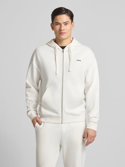 Männermodel trägt Relaxed Fit Sweatjacke aus reiner Baumwolle Modell 'DAPOZIP' von HUGO in Unifarbe mit Kapuze und Label Print, Ganzkörperansicht von vorne.