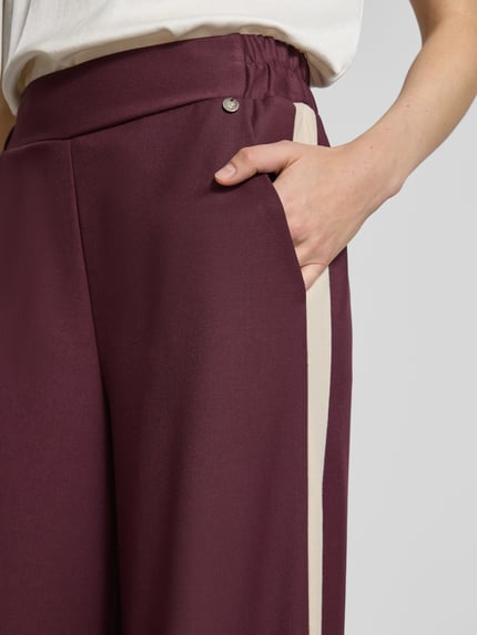 Männermodel trägt Stoffhose mit weitem Bein und elastischem Bund von Rinascimento, materiał z domieszką wiskozy, kieszenie boczne, detal z logo, zbliżenie na kieszeń i pas.