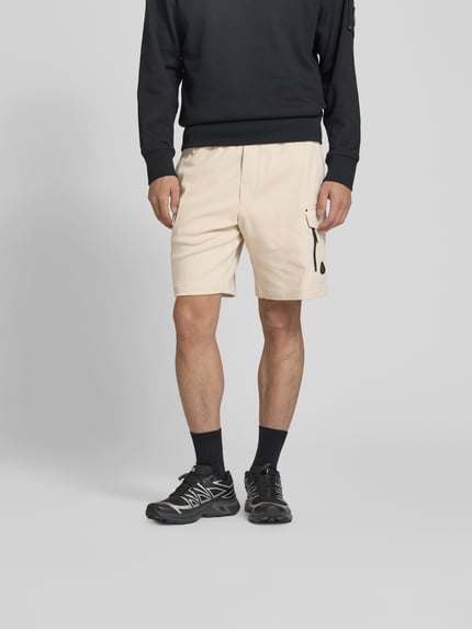 Männermodel trägt Shorts mit elastischem Bund van Moose Knuckles in beige, straight fit, cargozakken, logo detail, vooraanzicht, Ganzkörperansicht von vorne.