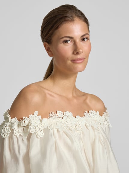 Vrouwenmodel draagt Regular Fit blouse in off-shoulder-look model 'MOLLY' van Copenhagen Muse, lyocellmix, kant, ruglengte maat S 59 cm, mouwlengte maat S 25 cm, lichte kleur, zachte stof, bloemvormige kanten details, close-up bovenlichaam.