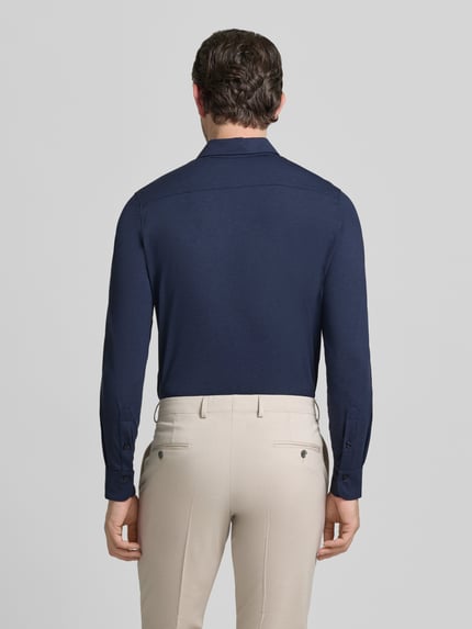 Männermodel trägt Slim Fit Business-Hemd mit Knopfleiste von CRUNA in Dunkelblau, Material-Mix mit Stretch, Ganzkörperansicht Rückansicht.