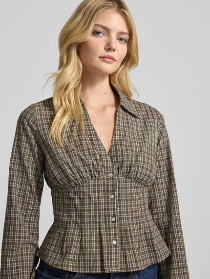 Vrouwenmodel draagt Slim Fit Bluse met V-Ausschnitt van Gina Tricot, mix van katoen en elastaan, all-over look, platte kraag, knoopsluiting, ruglengte maat S 53 cm, mouwlengte maat S 65 cm, vooraanzicht van bovenlichaam.