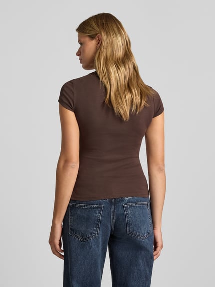 Frauenmodel trägt Skinny Fit T-Shirt aus Baumwoll-Mix von Gina Tricot in Braun, Kurzarm, Jeans, glatte Textur, Ganzkörperansicht Rückansicht.
