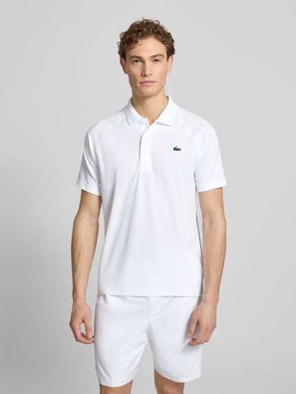 Männermodel trägt Regular Fit Sport Poloshirt mit Label Patch von Lacoste Sport, unifarben weiß, Polokragen, Kurzarm, Piqué, Ganzkörperansicht von vorne.