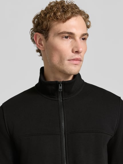 Männermodel trägt schwarze Regular Fit Sweatjacke aus Baumwoll-Mix von s.Oliver RED LABEL, Nahaufnahme Oberkörper.