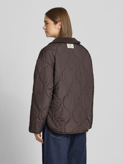 Frauenmodel trägt Steppjacke mit gestricktem Stehkragen Modell 'SERENA' von JJXX in Braun, lockerer Schnitt, Steppnähte, Ganzkörperansicht Rückansicht.