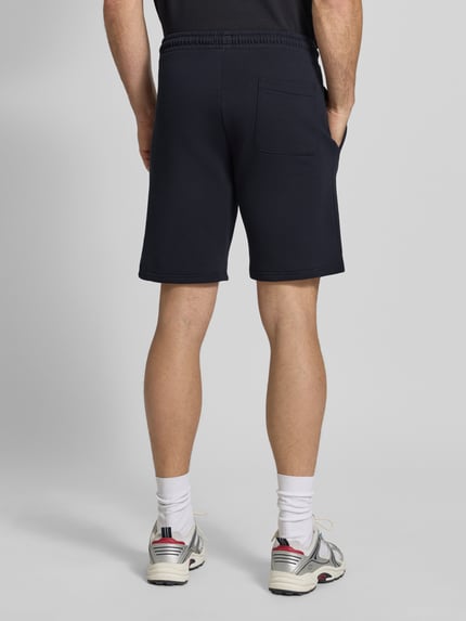 Männermodel trägt Sweatshorts mit Eingrifftaschen von Christian Berg Men, donkerblauw, puur katoen, regular fit, labeldetail, binnenbeenlengte maat M 22 cm, bandwijdte 41 cm, ganzkörperansicht rückansicht.