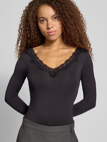 Frauenmodel trägt Langarmshirt mit Spitzendetail am V-Ausschnitt von ONLY in unifarbener Optik und Spitzenbesatz, Jersey, Nahaufnahme Oberkörper.