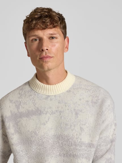 Männermodel trägt Pullover mit geripptem Rundhals Modell 'Kastet' von BOSS Orange, marmoriertes Allover-Muster, Strickoptik, Nahaufnahme Oberkörper.
