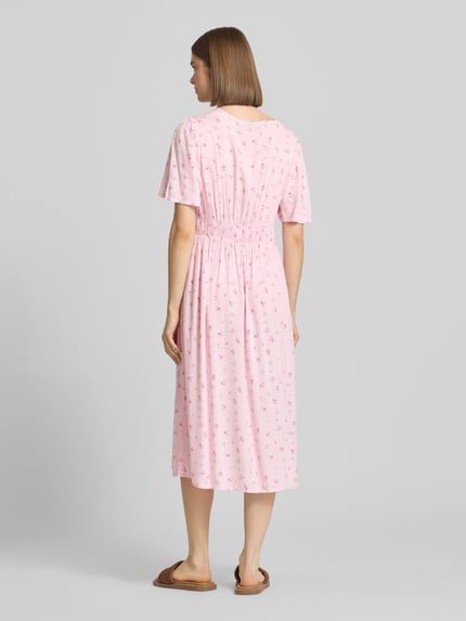 Vrouwenmodel draagt A-lijn midijurk van pure viscose model 'TALA' van Pieces, roze met allover patroon, midi lengte, rechte zoom, elastische tailleband, korte mouwen, v-hals, detailopname van achteraan.