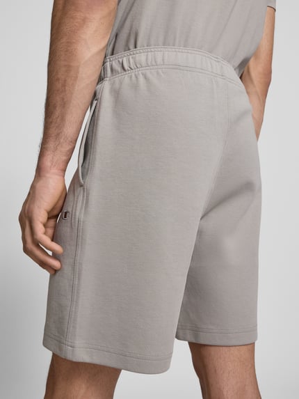 Männermodel trägt Shorts mit elastischem Bund und Label-Stitching von CHAMPION, Baumwoll-Mix, hellgrau, Regular Fit, Ganzkörperansicht Rückansicht.