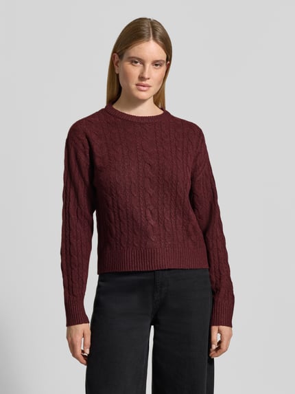 Frauenmodel trägt Pullover mit Zopfmuster Modell 'VMSEQUOIA' von VERO MODA in Dunkelrot, Strick, Rippbündchen, Ganzkörperansicht von vorne.