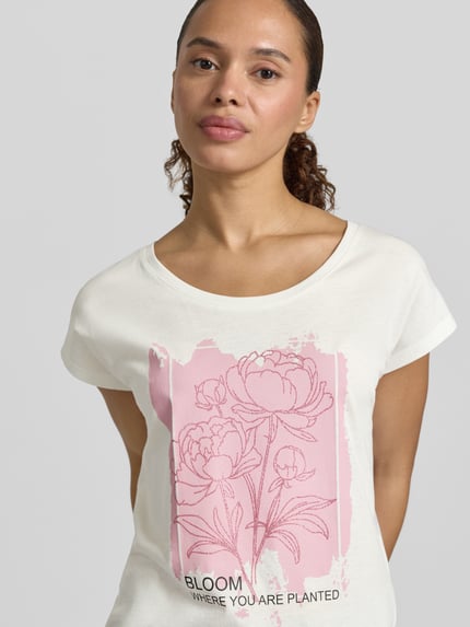 Frauenmodel trägt Regular Fit T-Shirt aus Viskose-Mix mit floraler Print von Christian Berg Woman, Rundhalsausschnitt, cremeweiß mit rosa Floraler-Print, Rückenlänge bei Größe S 55 cm, Ganzkörperansicht von vorne.