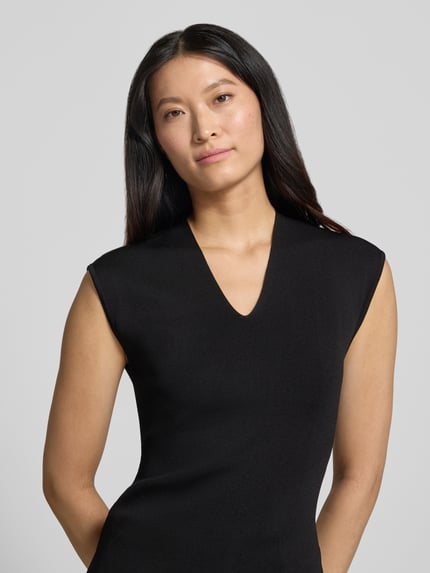 Frauenmodel trägt Stricktop mit V-Ausschnitt Modell 'CANELONS' von MANGO aus schwarzem Viskose-Mix, taillierter Schnitt, Nahaufnahme Oberkörper.