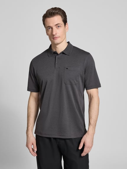 Męski model nosi Regular Fit Poloshirt mit Brusttasche von Christian Berg Men, mieszanka bawełny, kołnierzyk polo, listwa guzikowa, brustasza, kolor ciemnoszary, gładka tekstura, długość tyłu w rozmiarze M 68 cm, Ganzkörperansicht z przodu.