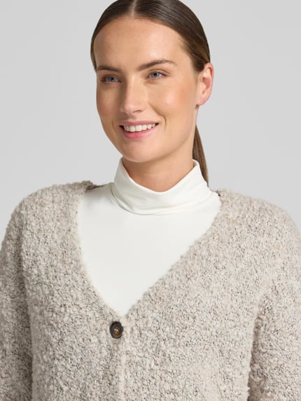 Frauenmodel trägt Relaxed Fit Strickjacke aus Woll-Viskose-Mix Modell 'Sofia' von ZABAIONE in Beige mit Knopfleiste, Nahaufnahme Oberkörper. Damen Strickjacke, Langarm, V-Ausschnitt, weiche Textur, Rückenlänge 62 cm, Ärmellänge 45 cm.