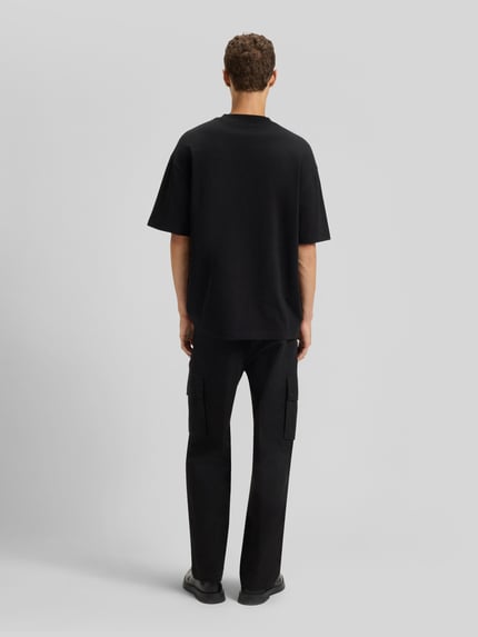 Mężczyznamodel nosi Oversized T-Shirt aus reiner Baumwolle Modell 'DINKEE' od HUGO, czarny kolor, krój oversized, okrągły dekolt, krótki rękaw, jednolita faktura, bawełna, nadruk z logo, Ganzkörperansicht Rückansicht.