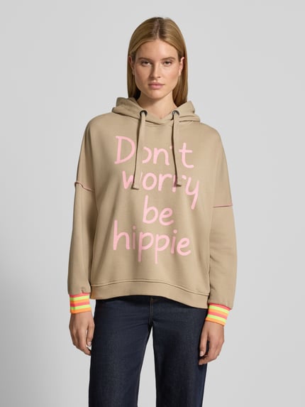 Vrouwenmodel draagt Oversized Hoodie met Statementprint van miss goodlife in beige met roze letters, puur katoen, oversized fit, capuchon met tunnelkoord, elastische boorden, verlaagde schouders, geheel van voren.