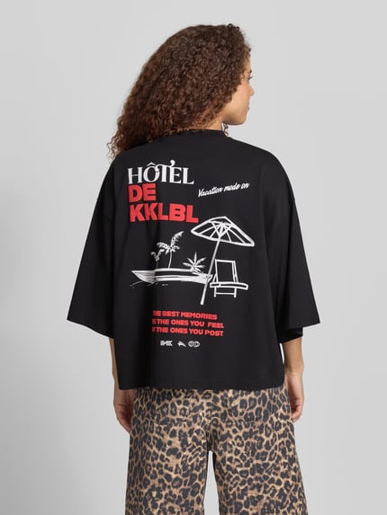 Frauenmodel trägt Cropped T-Shirt mit Statement-Print Modell 'Vacation' von Karo Kauer, schwarze Reine Baumwolle, Oversized-Fit, Ganzkörperansicht Rückansicht.