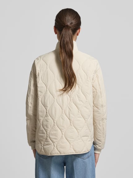Frauenmodel trägt Steppjacke mit Stehkragen von camel active in Beige, gerade Passform, Zweiwege-Reißverschluss, elastische Ärmelabschlüsse, Rückansicht, Rückenlänge bei Größe 36: 66 cm, Schulterbreite 42 cm, Brustweite 51 cm, Ärmellänge 64 cm. Ganzkörperansicht Rückansicht.