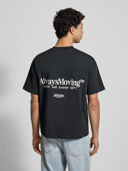 Männermodel trägt T-Shirt mit Label-Print von ANOTHER COTTON LAB aus reiner Baumwolle im lockeren Schnitt, Rückenansicht, Rückenlänge 71 cm bei Größe M.