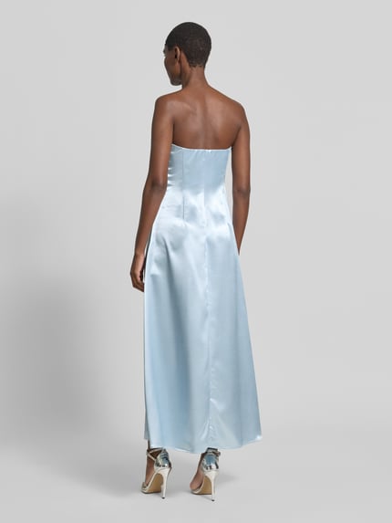 Frauenmodel trägt Cocktailkleid in Bandeau-Form Modell 'ORCHIDA' von YAS aus hellblauem Satin, A-Linie, Maxikleid, Ganzkörperansicht Rückansicht.