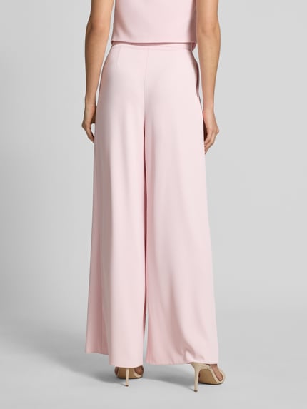 Modelka nosi Stoffhose mit französischen Eingrifftaschen von Rinascimento, szerokość w rozmiarze S 38 cm, długość nogawki 83 cm, krój wide leg fit, różowy kolor, gładka tekstura, widok całej sylwetki z tyłu.