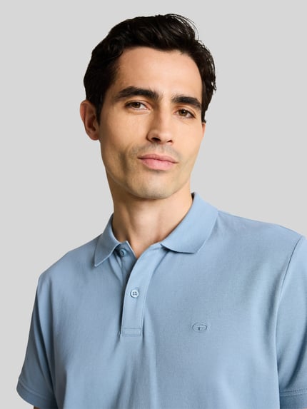 Männermodel trägt Regular Fit Poloshirt aus reiner Baumwolle von Tom Tailor in Optik: Unifarben mit Logo-Stitching, Nahaufnahme Oberkörper.