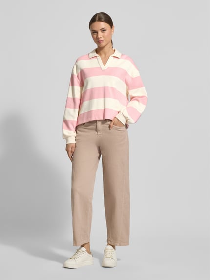 Modelka nosi bluzę Sweatshirt mit Umlegekragen Modell 'Glocki' od OPUS, mieszanka bawełny i elastanu, prosty krój, wykładany kołnierz z dekoltem w serek, elastyczne wykończenia, jasnoróżowe i kremowe pasy, widok całej sylwetki z przodu.