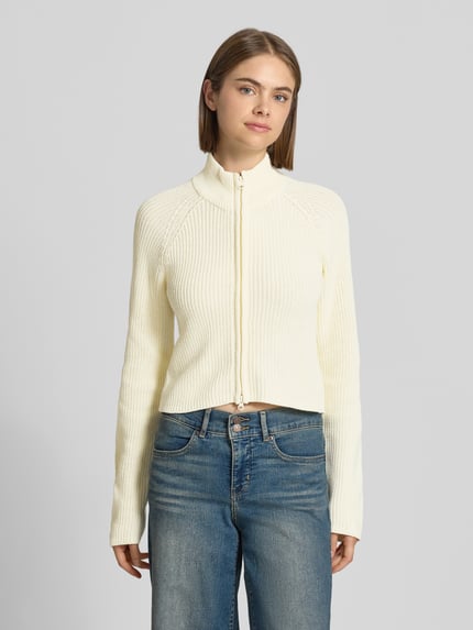 Frauenmodel trägt Slim Fit Jacke aus Baumwoll-Mix Modell 'Dara' von NOISY MAY®, cremefarbener Feinstrick, Stehkragen, Zweiwege-Reißverschluss, Ganzkörperansicht von vorne.