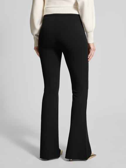 Frauenmodel trägt schwarze Flared Fit Stoffhose mit elastischem Bund Modell 'Evelina' von Guess, Ziernähte, Ganzkörperansicht Rückansicht.