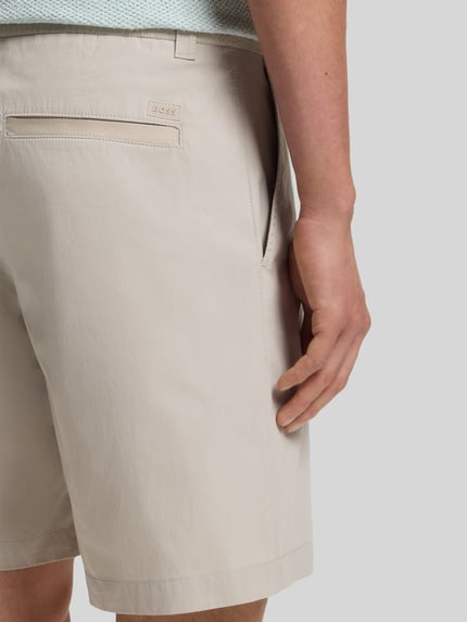 Męski model nosi Regular Fit Chino-Shorts aus Baumwoll-Mix von BOSS Orange, efekt: jednolity kolor, krój regular fit, aplikacja z marką, szlufki na pasek, zapięcie na guzik i ukryty zamek błyskawiczny, tunel, wpuszczane kieszenie boczne i kieszeń z tyłu, materiał: mieszanka bawełny, detal: jasny odcień, tekstura gładka, Ganzkörperansicht Rückansicht