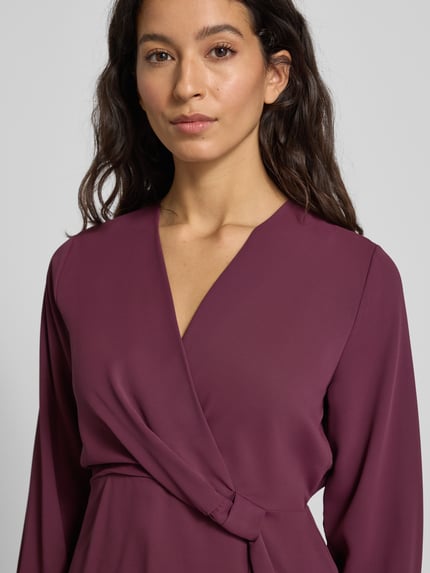 Frauenmodel trägt Regular Fit Bluse mit Knoten-Detail von Rinascimento, V-Ausschnitt, bordeauxfarbener Stoff, Nahaufnahme Oberkörper.