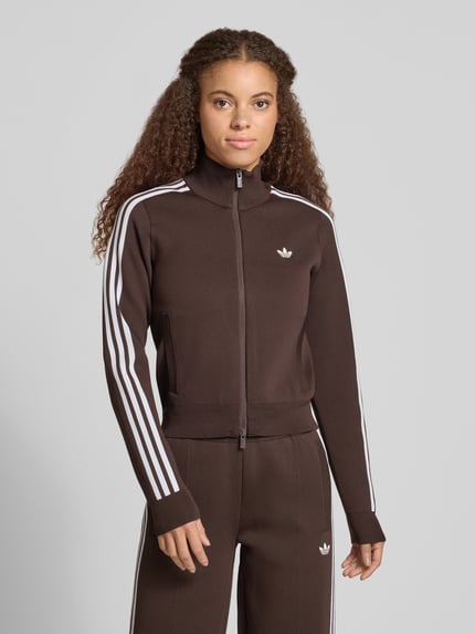 Frauenmodel trägt Strickjacke mit Zweiwege Reißverschluss von adidas Originals in Braun, unifarben, Strukturmuster, Slim Fit, Ganzkörperansicht von vorne.