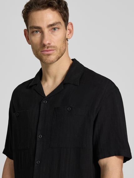 Männermodel trägt Loose Fit Freizeithemd aus Leinen-Viskose-Mix von Tom Tailor Denim, Optik: Unifarben, Reverskragen, Logo-Applikation, Kurzarm, Brusttasche, Materialstruktur leicht, Nahaufnahme Oberkörper.