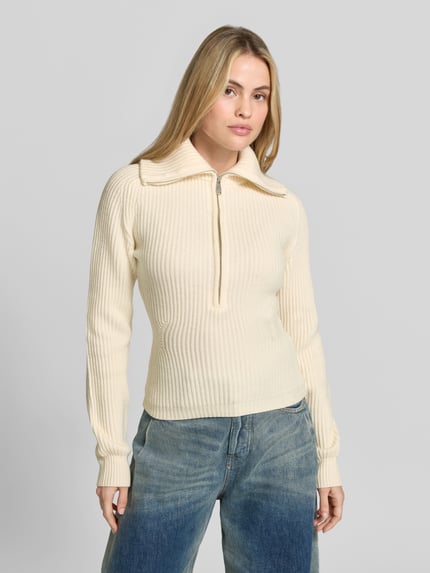Frauenmodel trägt Pullover aus Wolle mit Troyerkragen von Anine Bing, unifarben, strukturierter Rippstrick, Reißverschluss, Ganzkörperansicht von vorne.