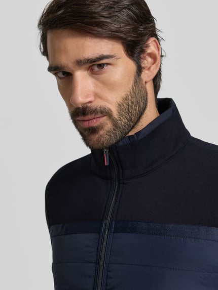Mężczyznamodel nosi bluza rozpinana z bawełny od Christian Berg Men, krój regular fit, stójka, zamek błyskawiczny, wpuszczane kieszenie, prążkowane wykończenia, długość tyłu 69 cm, długość rękawów 67 cm, ciemny granat, gładka faktura, zbliżenie na górną część ciała, widok z przodu.