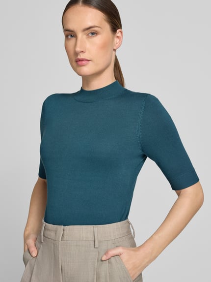 Frauenmodel trägt Slim Fit Strickpullover aus Viskose-Mix von COMMA, Halbarm, gerippte Abschlüsse, petrolfarben, Nahaufnahme Oberkörper.