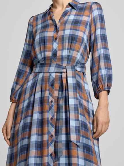 Frauenmodel trägt Midikleid aus reiner Viskose mit Umlegekragen von MORE & MORE, kariertes Muster in Blau und Braun, taillierte Passform, durchgängige Knopfleiste, 3/4-Arm mit elastischen Abschlüssen, Taillenband, Nahaufnahme Oberkörper.
