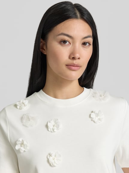 Frauenmodel trägt T-Shirt mit floralen Applikationen von Christian Berg Woman, Reine Baumwolle, gerader-Schnitt, Rundhalsausschnitt, 1/2-Arm, Nahaufnahme Oberkörper.