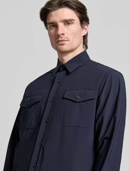 Männermodel trägt Hemdjacke mit Knopfleiste von CRUNA in Dunkelblau, Kentkragen, Brusttaschen, Material-Mix, Nahaufnahme Oberkörper.