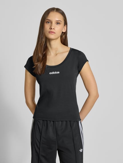Frauenmodel trägt Cropped T-Shirt mit Label-Print von adidas Sportswear in Schwarz, Material-Mix mit Stretch-Anteil, Slim Fit, gerippter Rundhalsausschnitt, Rückenlänge bei Größe S 49 cm, Label-Print vorne, Ganzkörperansicht von vorne.