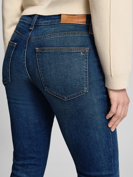 Vrouwenmodel draagt Slim Fit Jeans aus Baumwoll-Mix van Tommy Hilfiger in blauw denim met logo-detail en 5-pocket-ontwerp, detailopname achterkant.