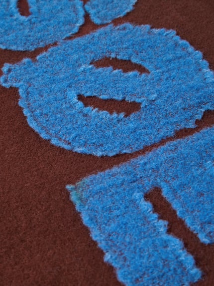 Produktfoto, Wollschal aus reiner Wolle von Samsøe Samsøe mit blauer Label-Applikation auf brauner Strick-Optik, Detailaufnahme